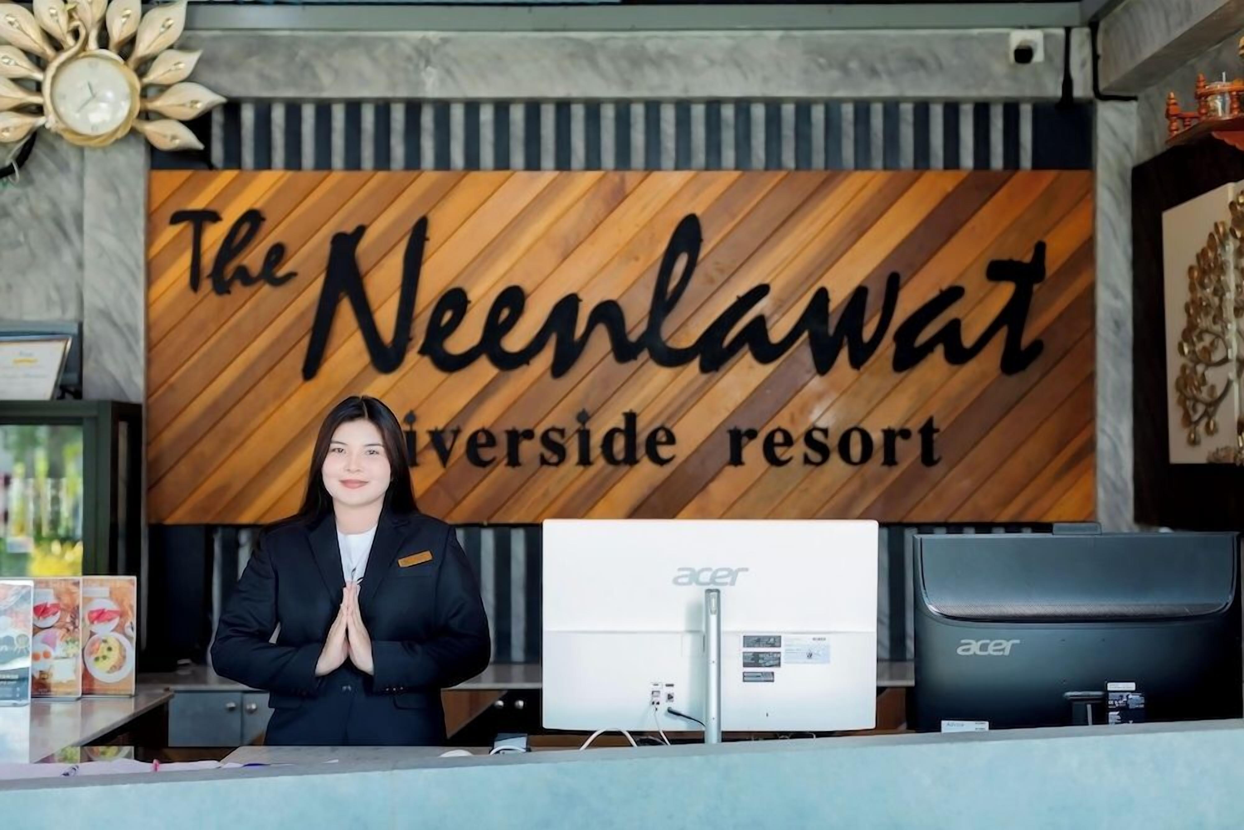 A reception desk at The Neenlawat Riverside Resort with a wooden sign, a computer, and a monitor.