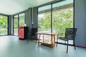 A modern room with a large window, a wooden table, a black chair, and a red cabinet. - The Neenlawat Riverside (Phunphin)