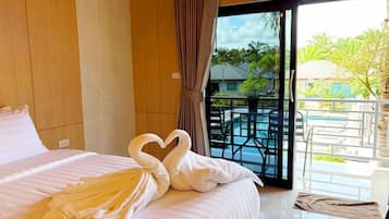 A hotel room with a bed, a balcony with a pool, and a view of the outdoors.