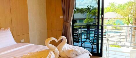 A hotel room with a bed, a balcony with a pool, and a view of the outdoors.