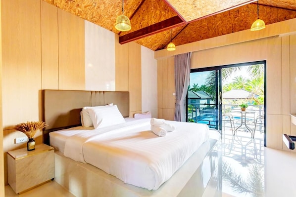 A hotel room with a large bed, a nightstand, a window with a view of a pool and palm trees, and a ceiling with wooden beams.