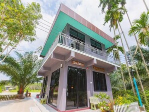 A two-story building with a balcony, surrounded by palm trees and greenery.