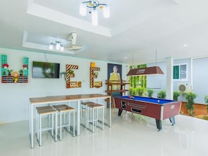 A modern kitchen with a pool table, bar stools, and a television. - The Neenlawat Riverside (Phunphin)