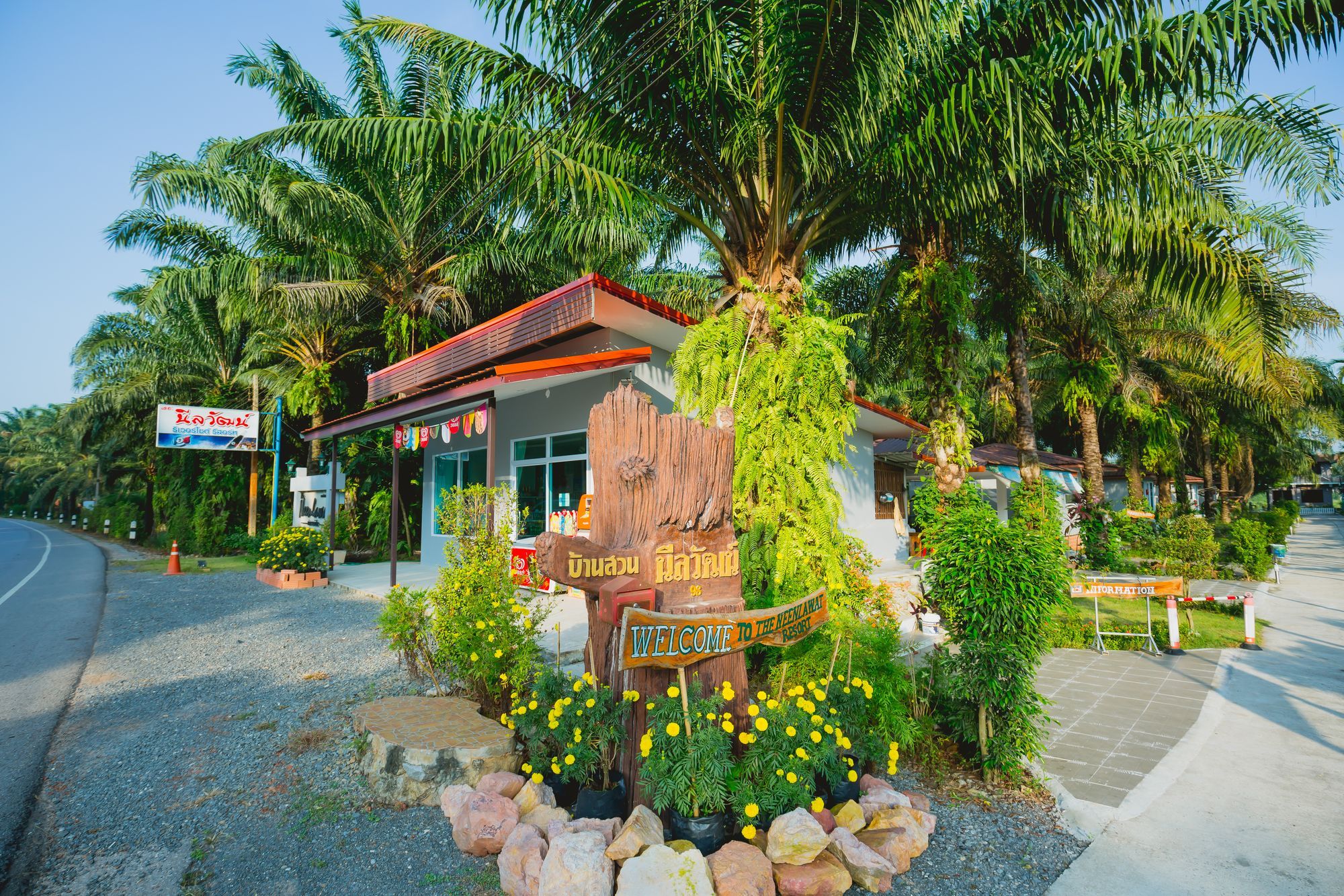 A resort entrance with a wooden sign, a building with a red roof, and tropical vegetation.