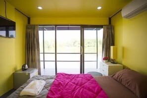 A room with a bed, a bedside table, a lamp, and a window with curtains. - Neenlawat Riverside (Phunphin)
