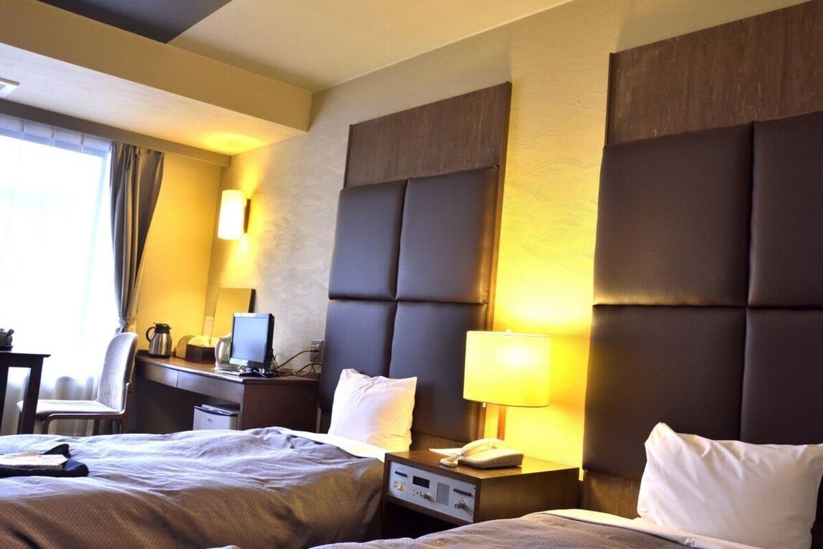 Ein Hotelzimmer mit zwei Betten, einem Schreibtisch, einem Stuhl, einer Lampe und einem Telefon.