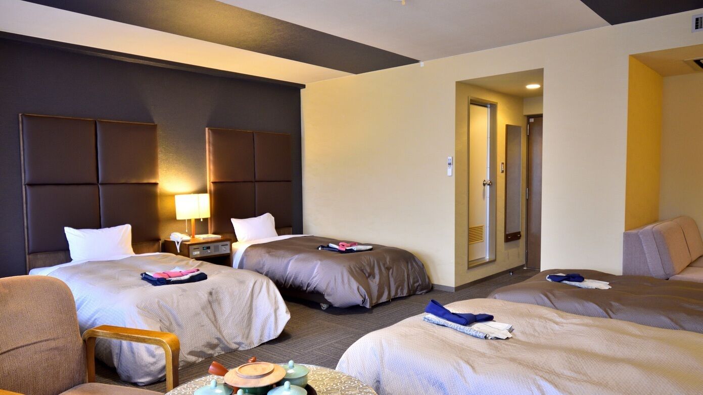 Habitación de hotel con dos camas, un escritorio, una silla y una puerta que da a otra habitación.