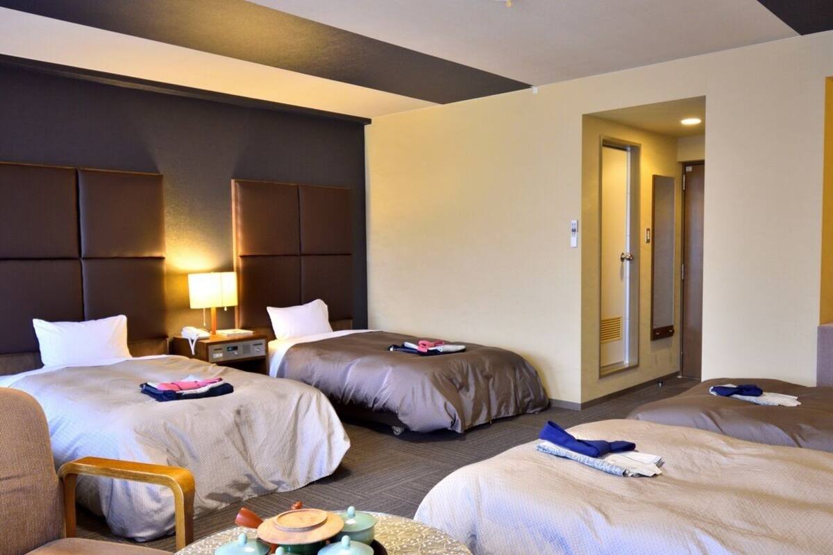 Ein Hotelzimmer mit zwei Betten, einem Schreibtisch, einem Stuhl und einer Tür zu einem weiteren Raum.