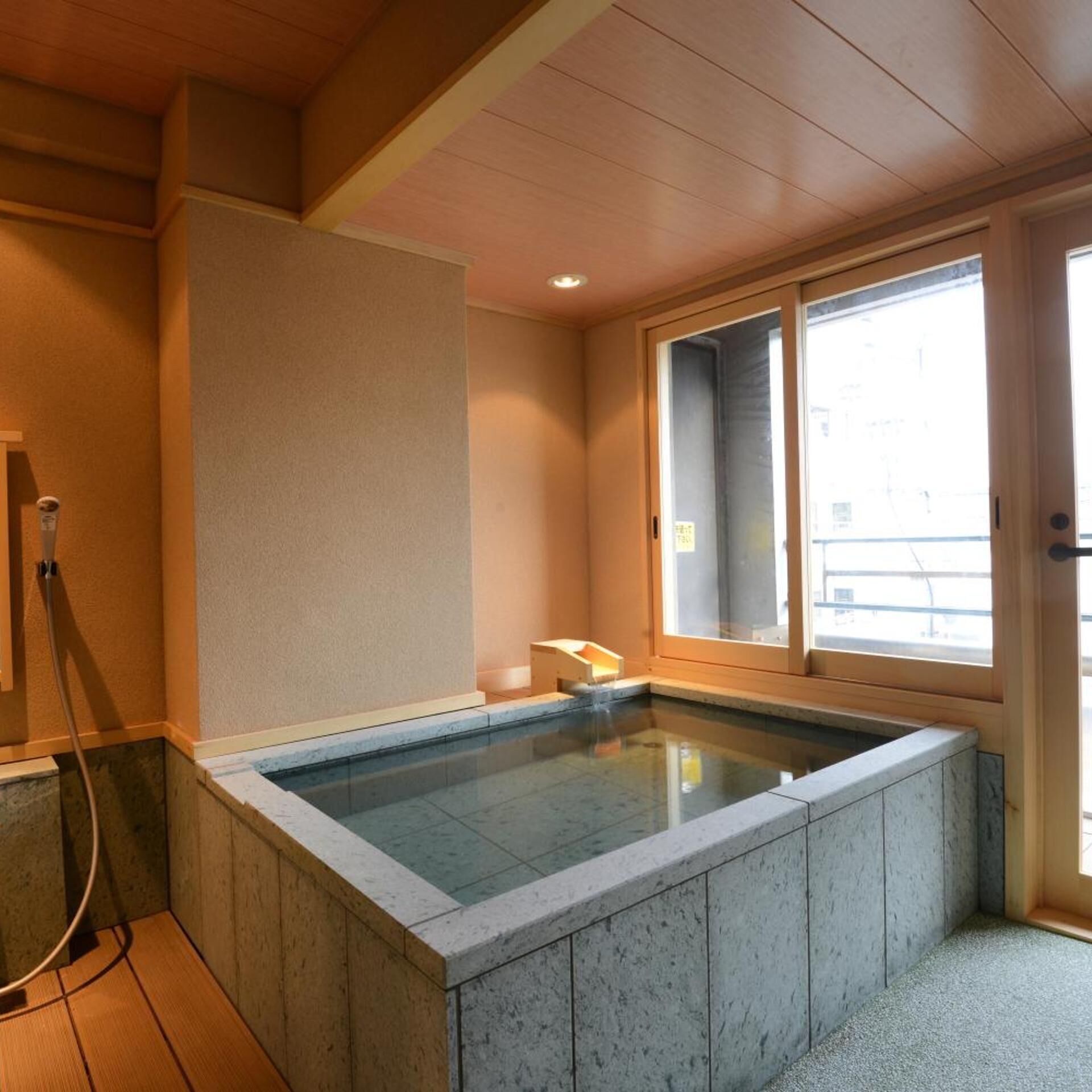 A room with a stone-lined hot tub, wooden beams, a window, and a door.