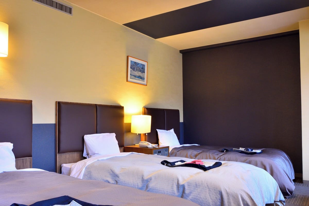 Ein Hotelzimmer mit zwei Betten, einem Nachttisch mit Lampe, einem gerahmten Bild an der Wand und einem großen Fenster.