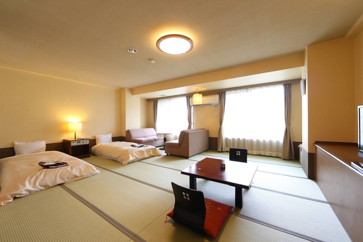 Ein Hotelzimmer mit Tatami-Boden, einer Couch, einem Tisch und einem Fernseher.
