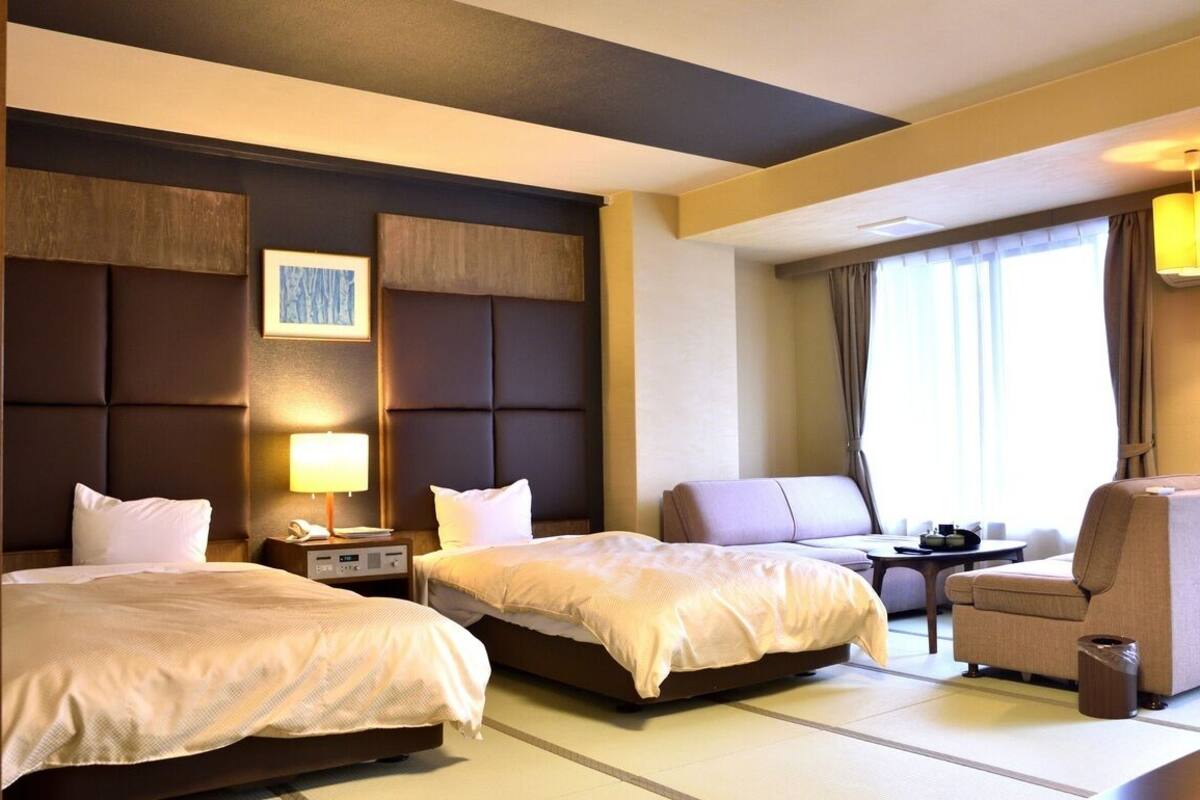 Ein Hotelzimmer mit zwei Betten, einem Schlafsofa, einem Sessel, einem kleinen Tisch und einer Lampe.