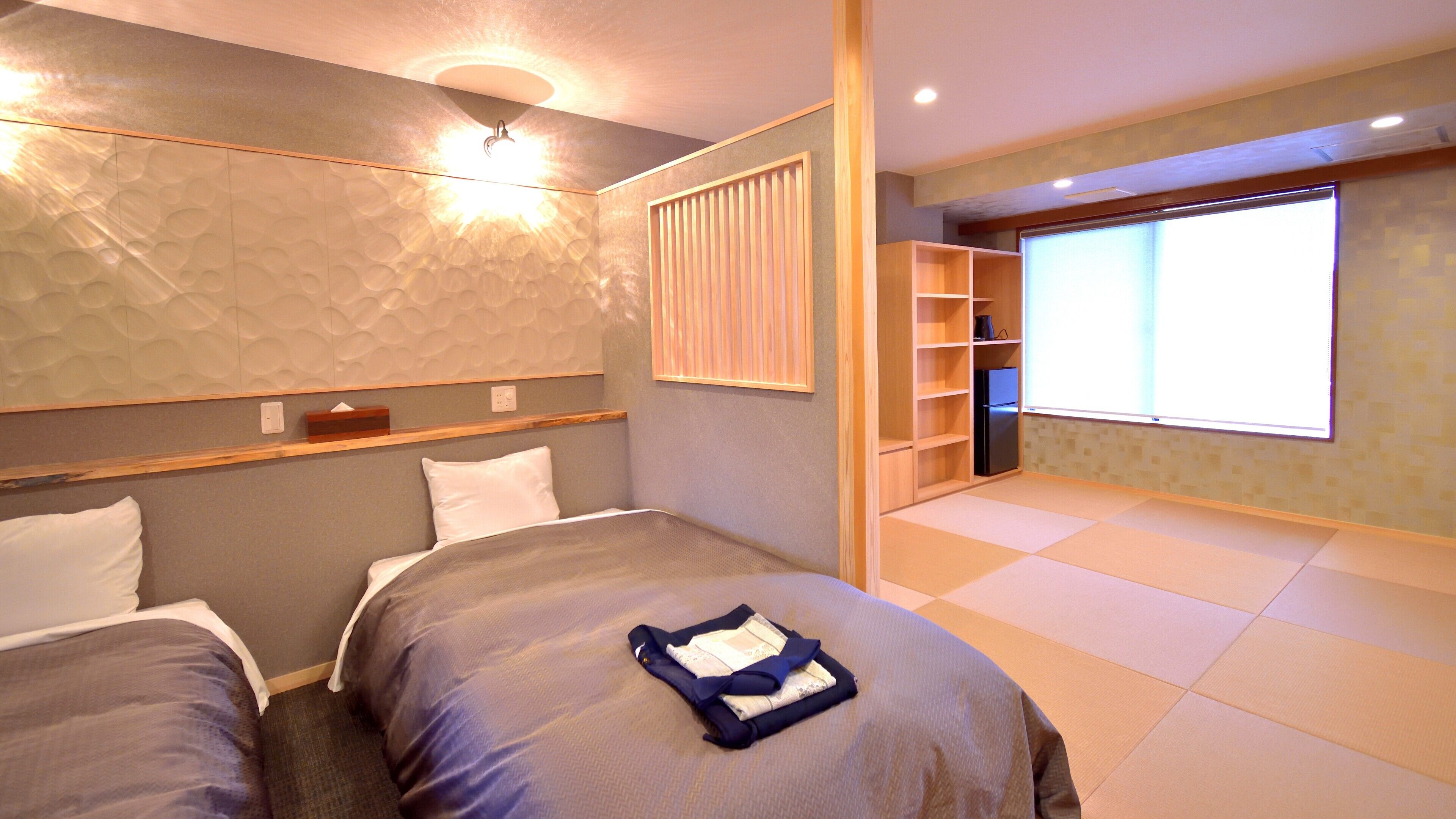 Habitación de hotel con dos camas, armario empotrado, ventana grande y lámpara fijada a la pared.