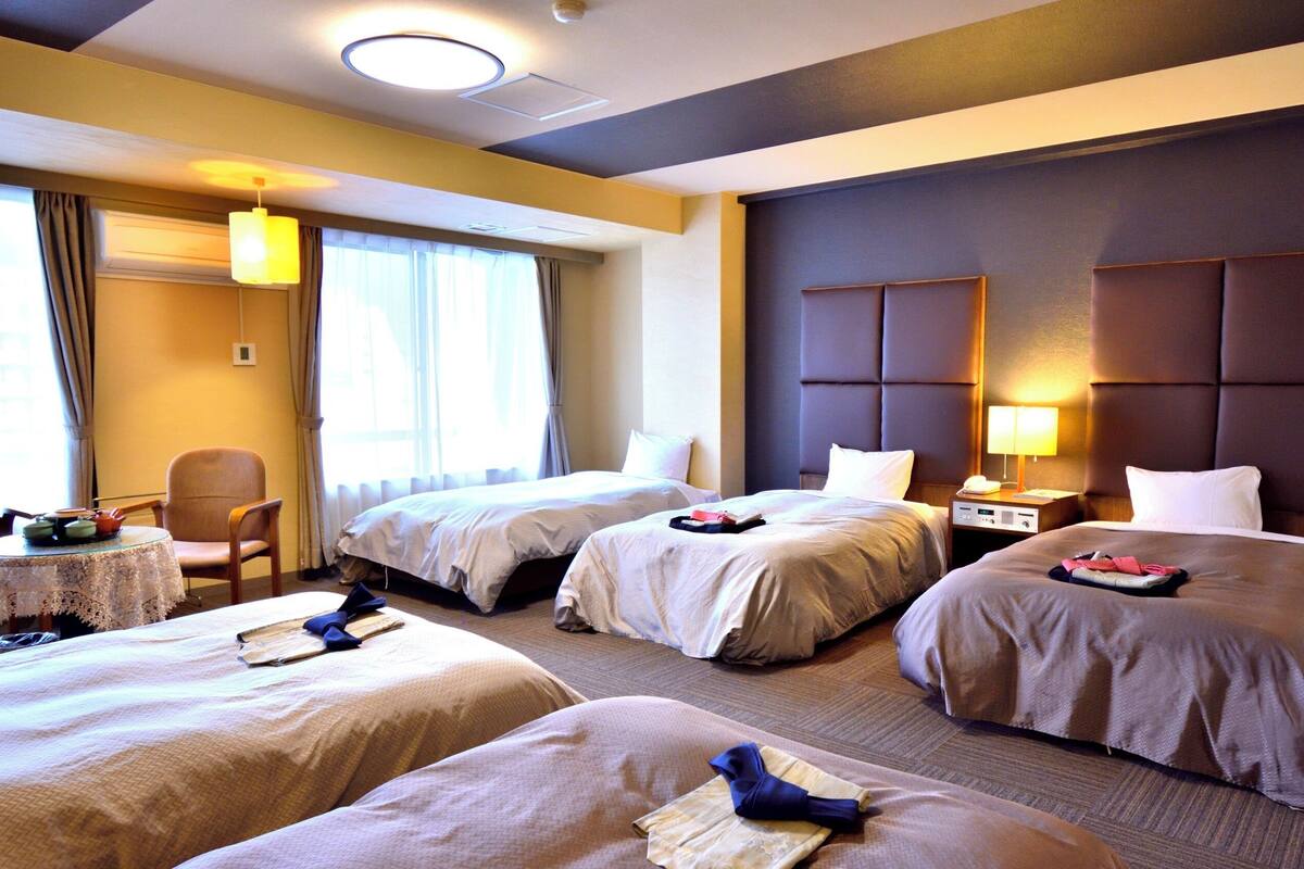 Ein Hotelzimmer mit zwei Betten, einem kleinen Tisch, einem Stuhl und einem Fenster mit Vorhängen.