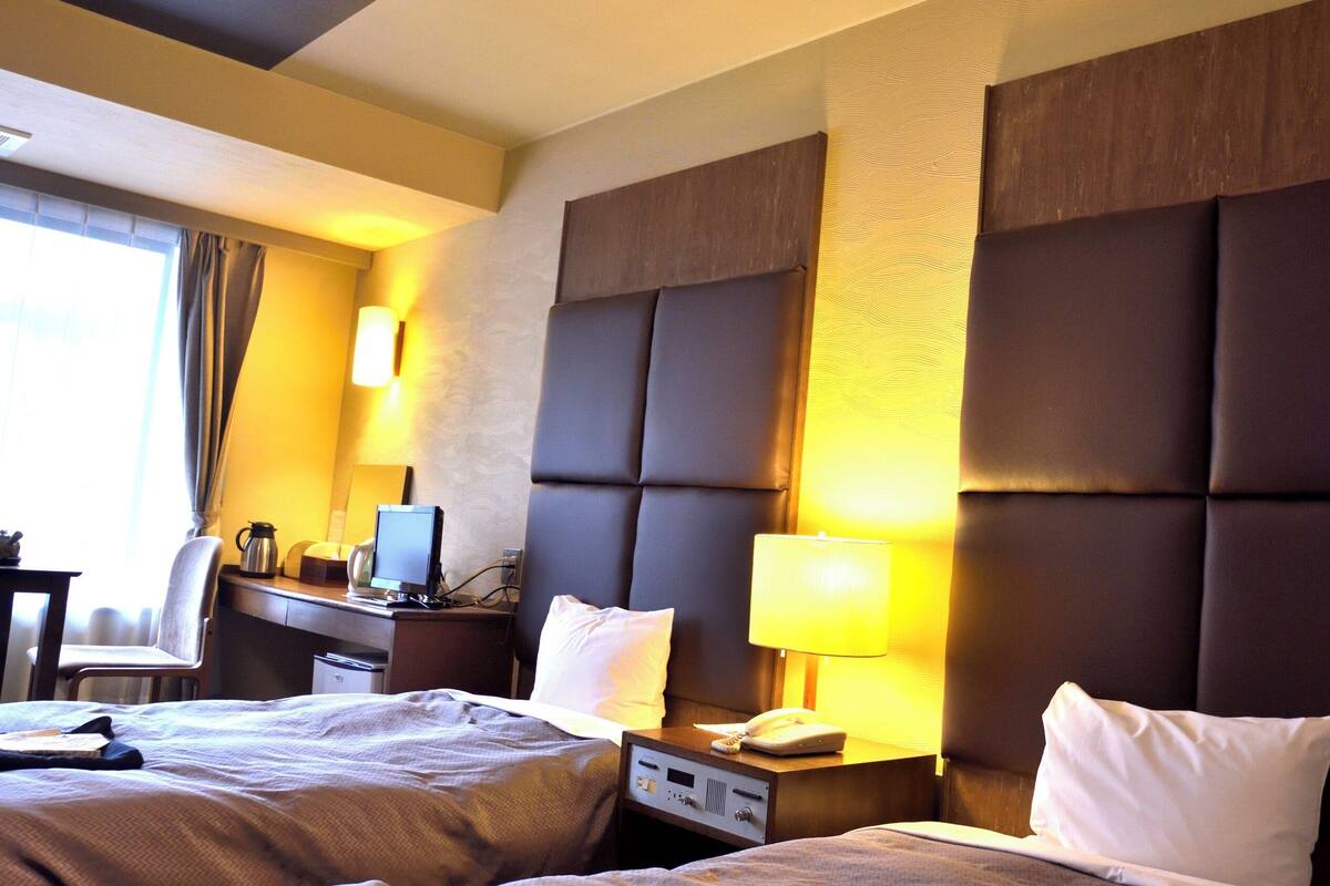 Ein Hotelzimmer mit einem großen Bett, einem Schreibtisch mit Computer, einem Stuhl und einer Lampe.