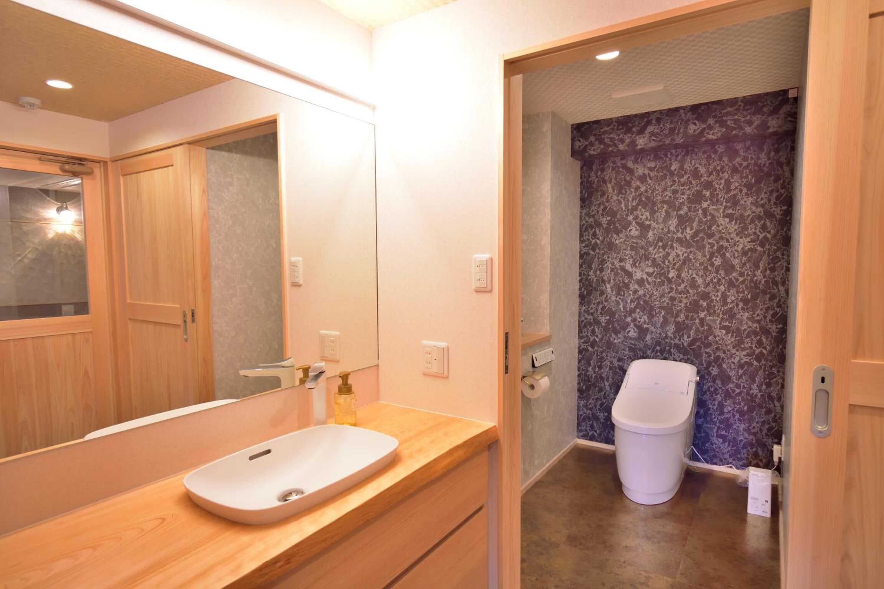Un baño moderno con tocador de madera, un lavabo blanco, un espejo y un inodoro con pared de estampado de mármol.