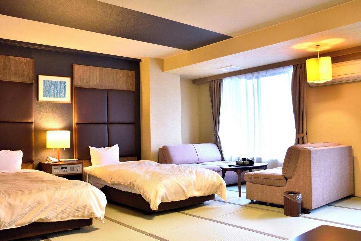Ein Hotelzimmer mit zwei Betten, einem Schreibtisch, einem Stuhl, einer Lampe und einem fenster mit Vorhängen.