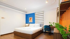 Habitación de hotel moderna con estructura de cama de madera, pared azul decorativa, ventana con persianas, escritorio con silla y planta en maceta.