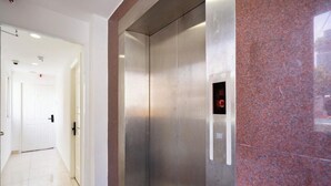 Un ascensor moderno con panel de control, junto a un pasillo con una puerta blanca y un revestimiento de pared de baldosas rojas.