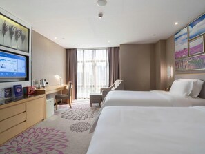 A hotel room with two beds, a desk, a chair, and a large window.