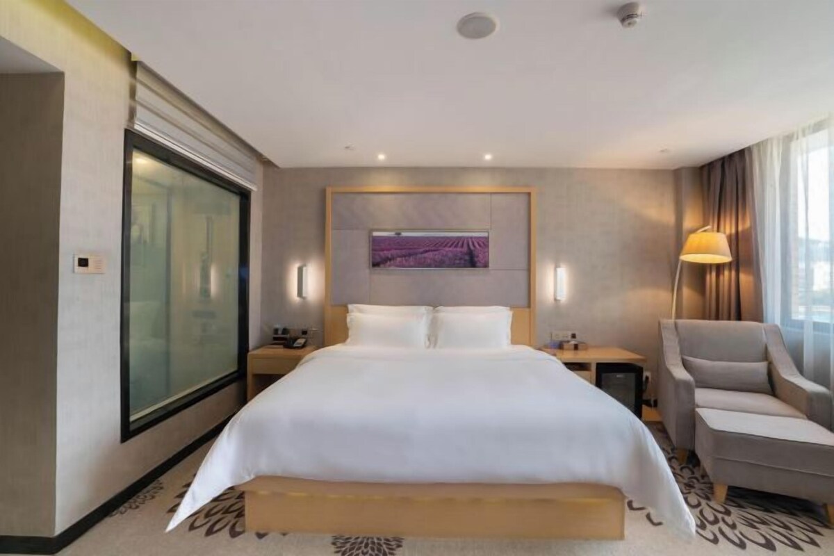 A hotel room with a large bed, a desk, a chair, a TV, and a window.