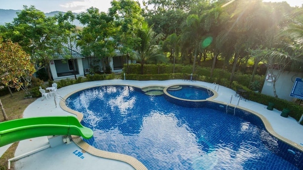 A swimming pool with a slide, surrounded by greenery and a view of hills. - Reindeer Park Resort (Nakhon Nayok)