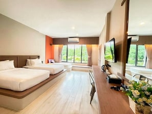 Ein Hotelzimmer mit einem großen Bett, einem kleineren Bett, einem Schreibtisch mit Stuhl, einem Fernseher und einem Fenster mit Vorhängen.