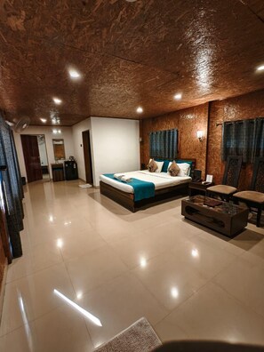 A spacious hotel room with a large bed, a sitting area, and a kitchenette. - Whispering Woods Resort-lonavala (Lonavala)