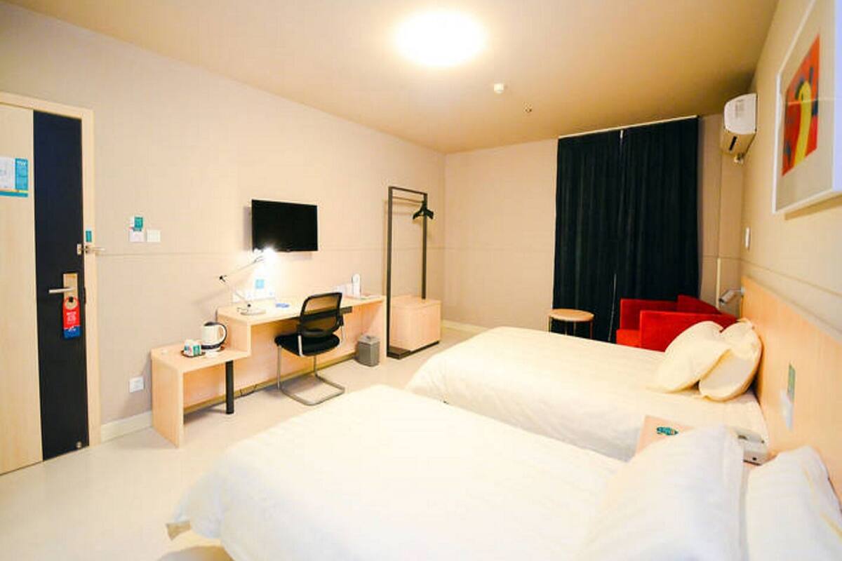 A hotel room with two beds, a desk with a chair, a mirror, a television, a wardrobe, and a bathroom with a shower.