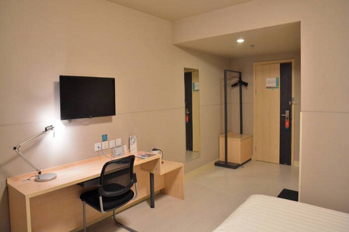 A hotel room with a desk, chair, bed, TV, and a mirror.