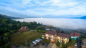 A residential area with houses, a small commercial building, and a view of a mountainous landscape with clouds. - Hotel Viewpoint Khao Koh (Khao Kho)