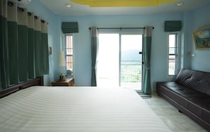 A hotel room with a bed, a sofa, a window with curtains, a nightstand, and a lamp.