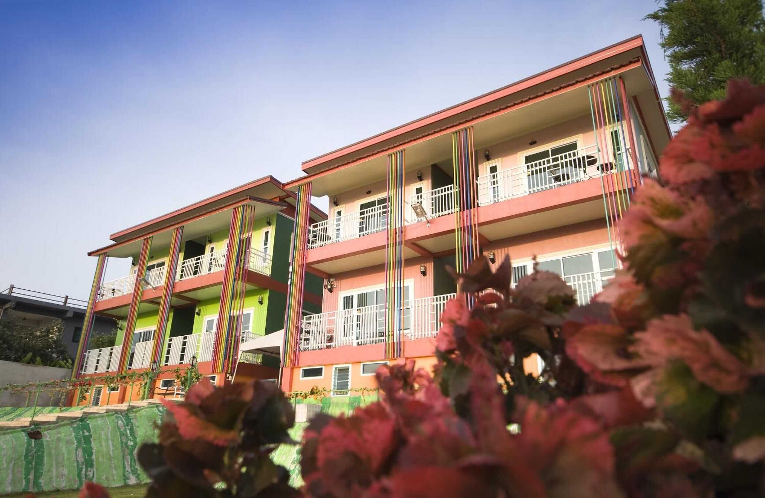 A multi-story building with balconies and a green fence in the foreground.