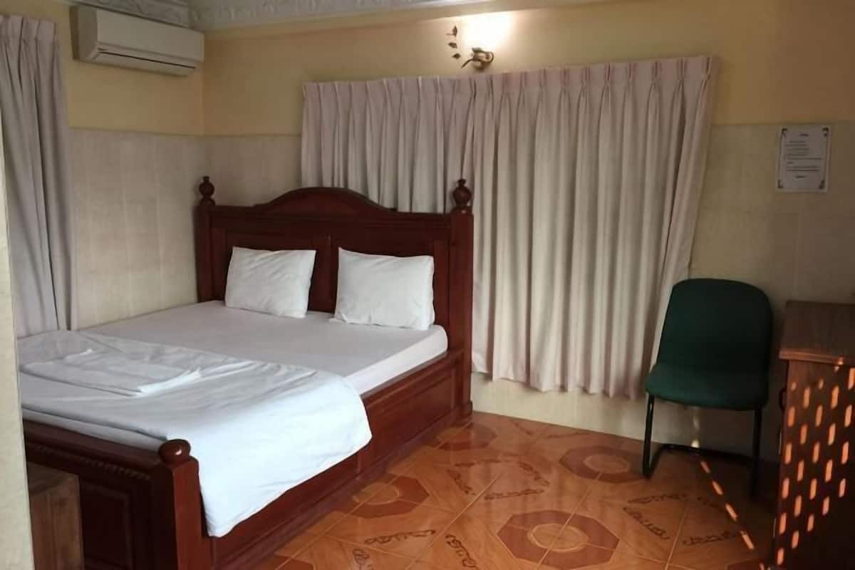 A room with a wooden bed, a green chair, a desk, and a window with curtains.