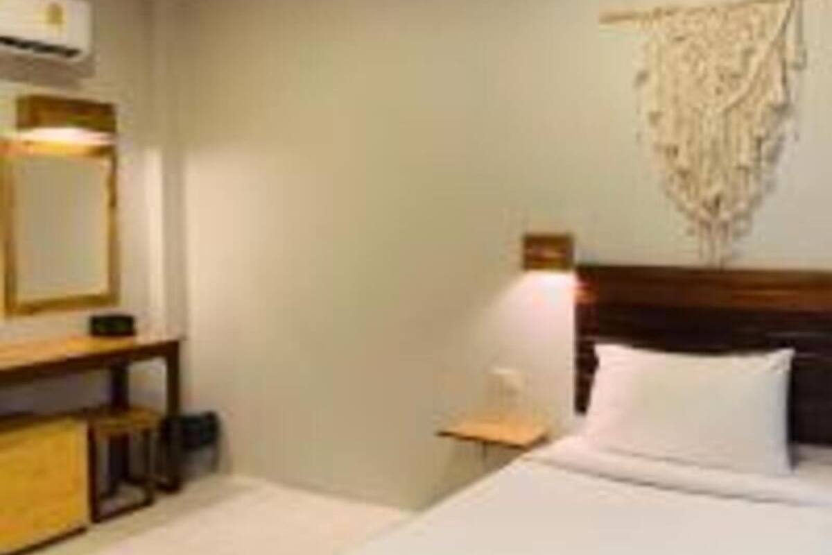 Een hotelkamer met een bed, een nachtkastje van hout, een bureau en een wandairconditioner.