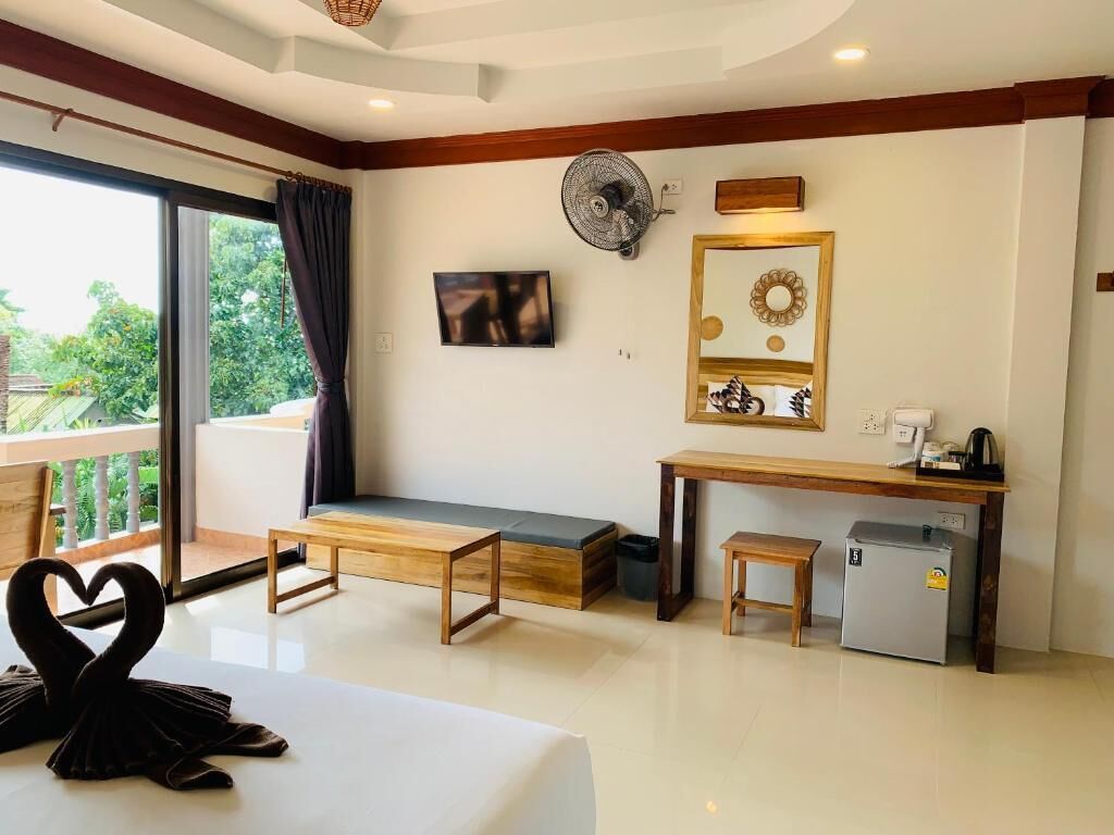 Habitación de hotel con balcón, una cama, un escritorio, un refrigerador pequeño y un banco.