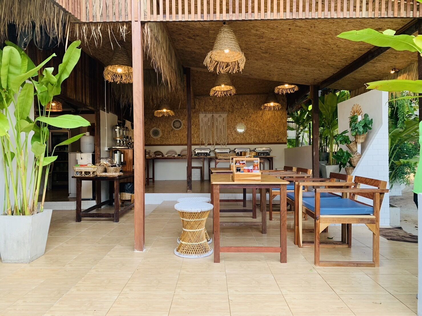 A rustic-style dining area with wooden tables and chairs, thatched ceiling, and hanging woven light fixtures.