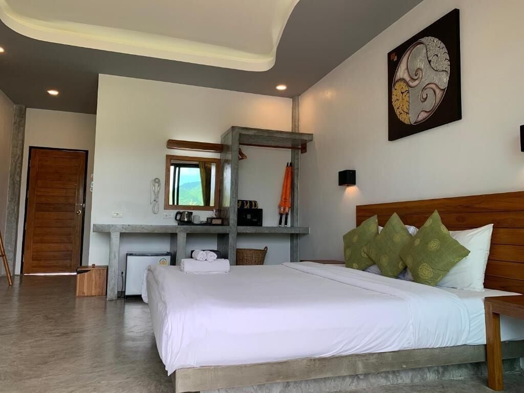 A bedroom with a large bed, a desk with a chair, a mirror, and a wall-mounted artwork.