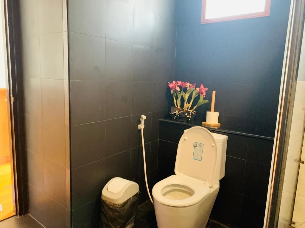 Et badeværelse med et hvidt toilet, en skraldespand og en toiletpapirholder fastgjort på væggen.