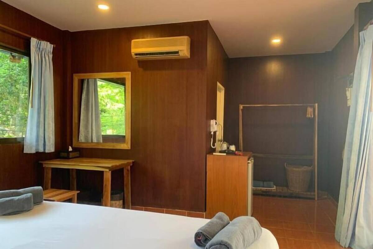 Hotelkamer met een bed, een bureau, een spiegel, een airconditioning en uitzicht op groen.