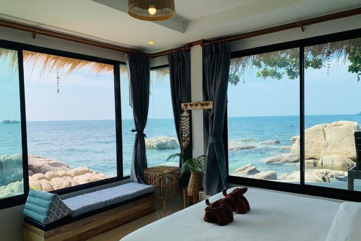 Een slaapkamer met een groot raam met uitzicht op zee, een bed, een nachtkastje en een zithoek met uitzicht op de oceaan.