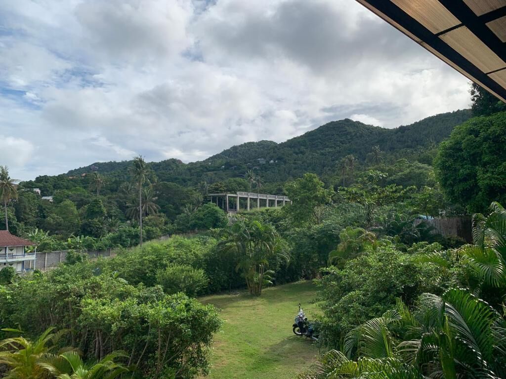 A lush green landscape with a hill, a building with a white facade, and a motorbike on a path.