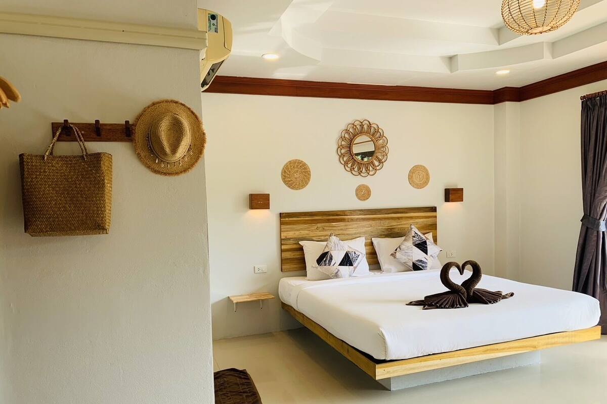 Een moderne slaapkamer met een houten hoofdbord, een bed met wit beddengoed, decoratieve spiegelwanden en een kussen in de vorm van een zwaan.