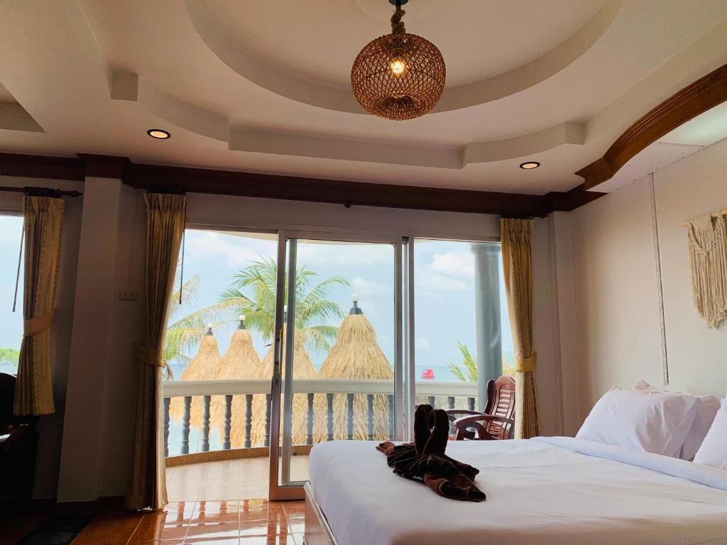 A hotel room with a bed, a chair, a balcony with a view of palm trees and a beach.