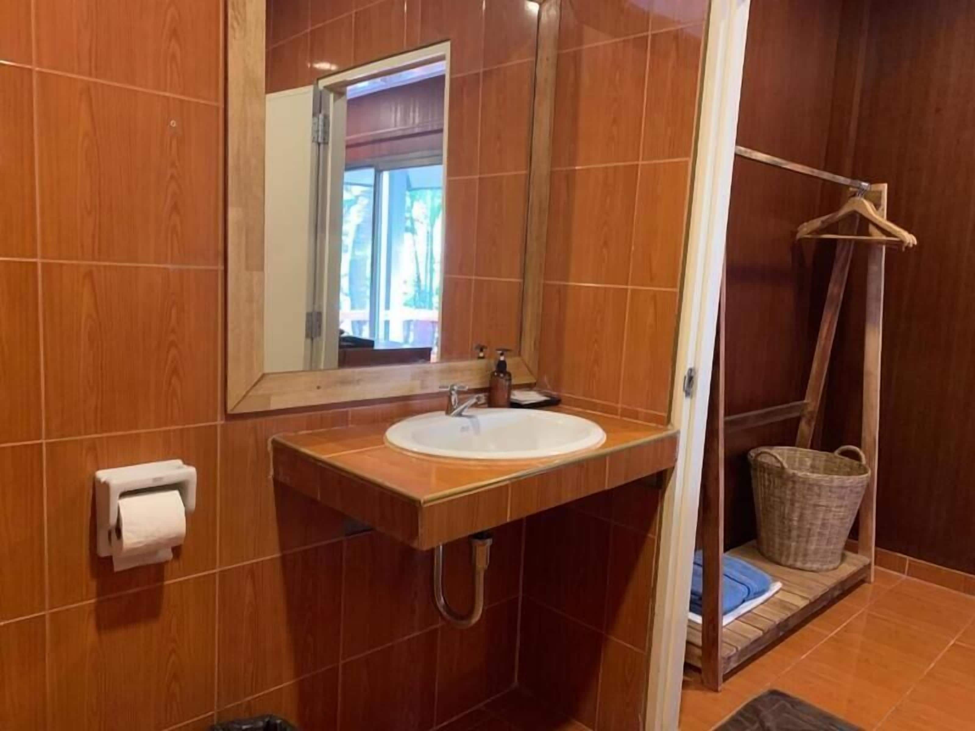 A bathroom with a wooden vanity, a sink, a mirror, and a shower area.