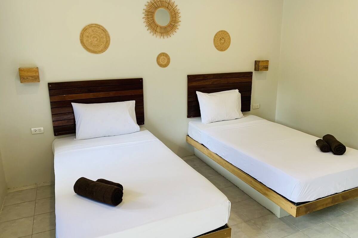 Twee eenpersoonsbedden met houten hoofdborden, wit beddengoed en decoratieve wandkunst.