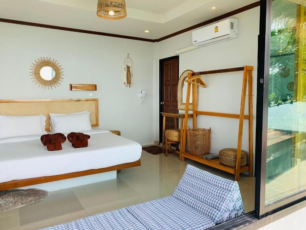A bedroom with a large bed, a bedside table, a chair, a shelf with baskets, and a view of the outdoors through a glass door.