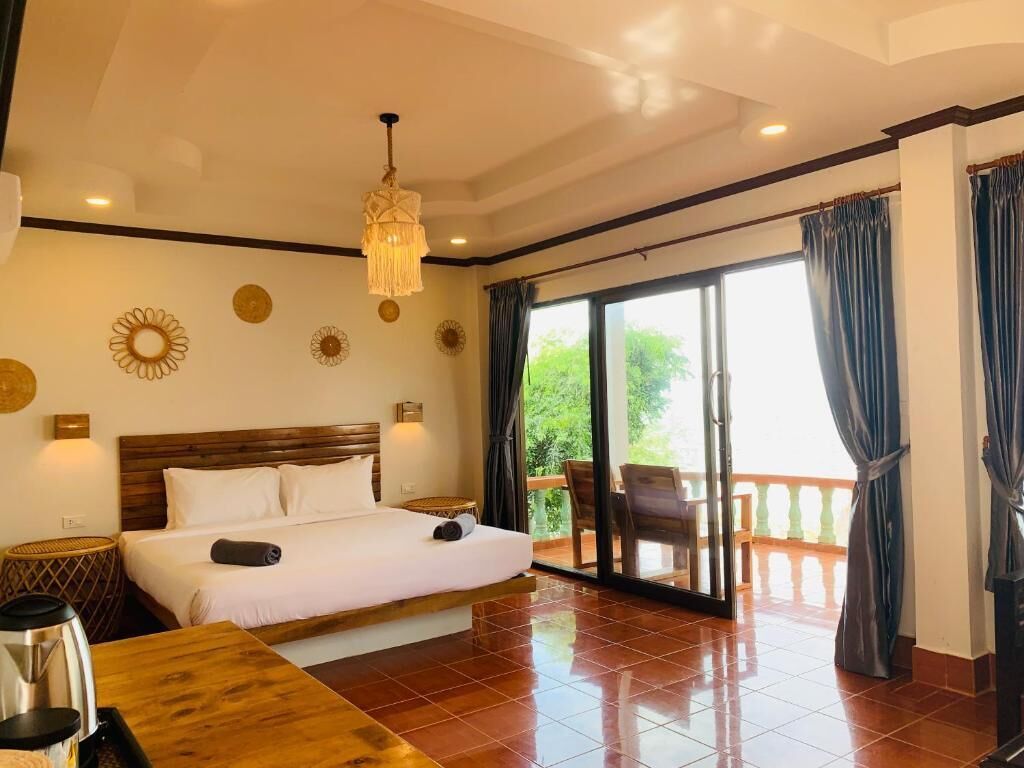 A hotel room with a large bed, a wooden headboard, a chandelier, a balcony with a view, and a sliding glass door.