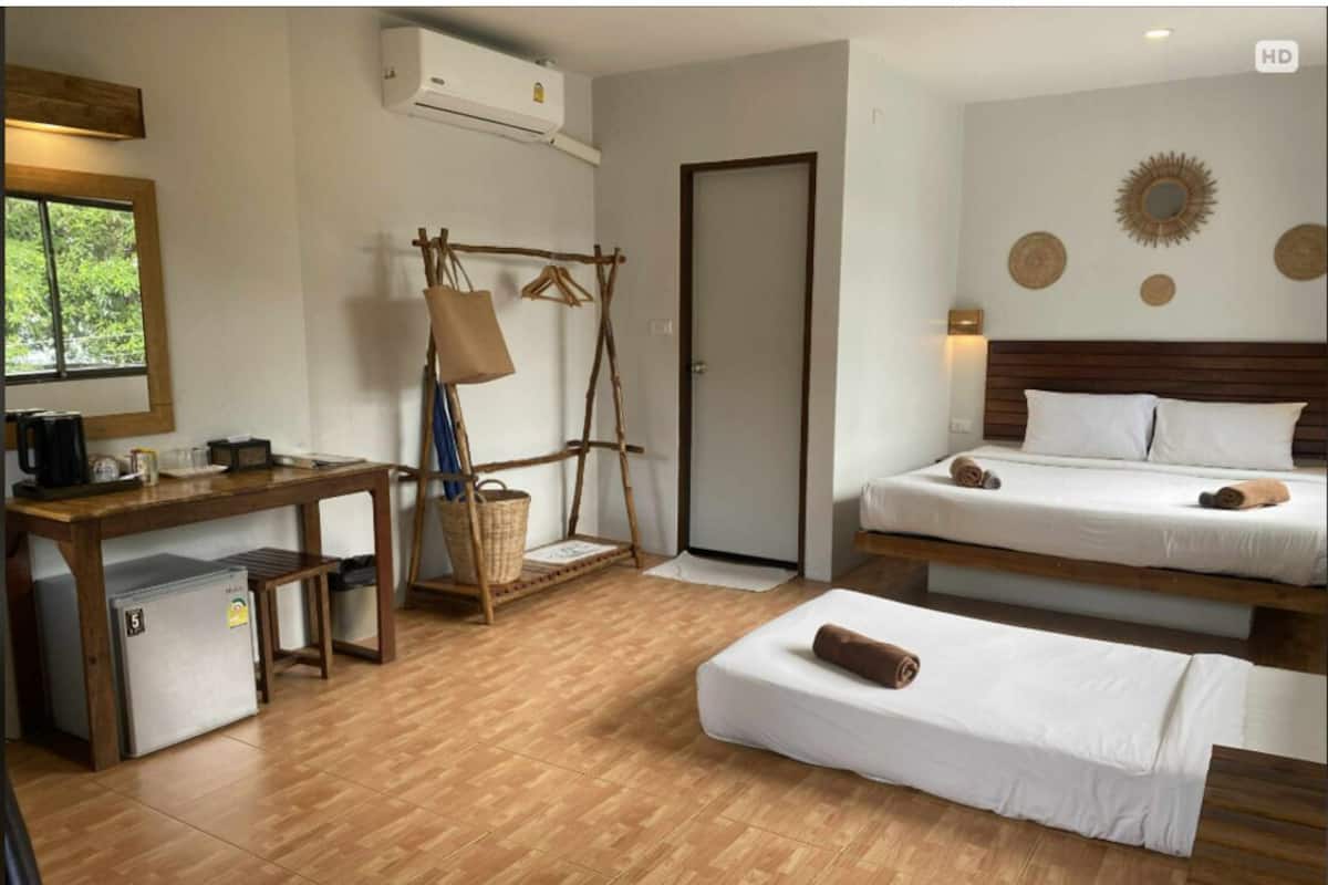 Een hotelkamer met een houten bureau, een kleine koelkast, een bed met een houten hoofdeinde en een wandairconditioner.