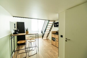 A compact kitchen with a wooden countertop, bar stools, and a staircase leading to an upper level.